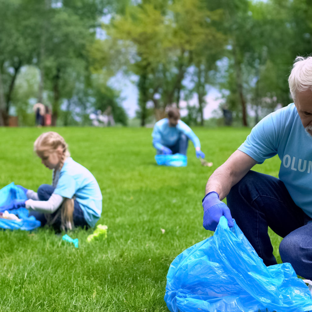 Senior man picking up litter in park together family smiling camera, earth care